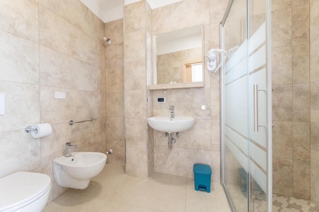 A bathroom with a toilet, bidet, sink, and glass shower enclosure.