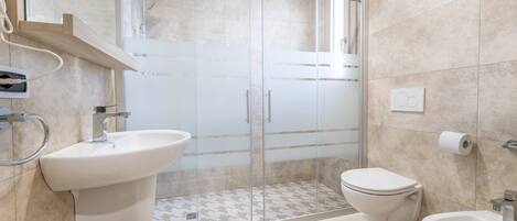 Un baño moderno con ducha de vidrio, lavamanos, un bidé y un inodoro.