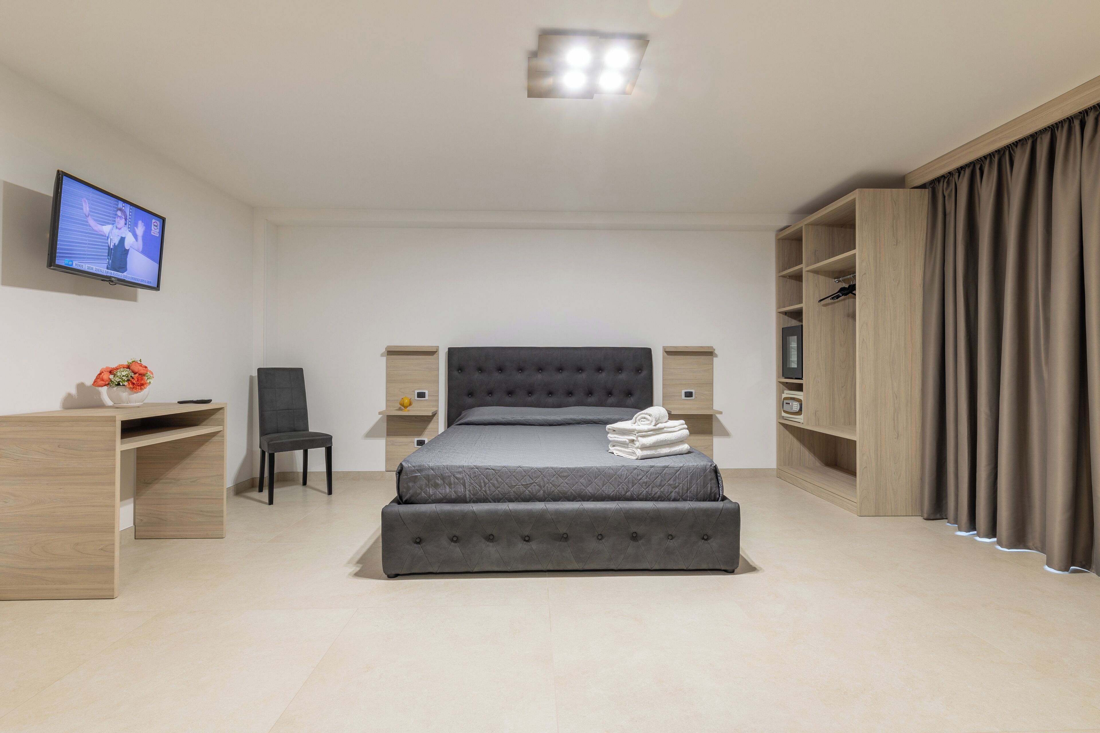 Une chambre d’hôtel moderne équipée d’un lit, d’un bureau, d’une chaise, d’une télévision et d’une armoire.