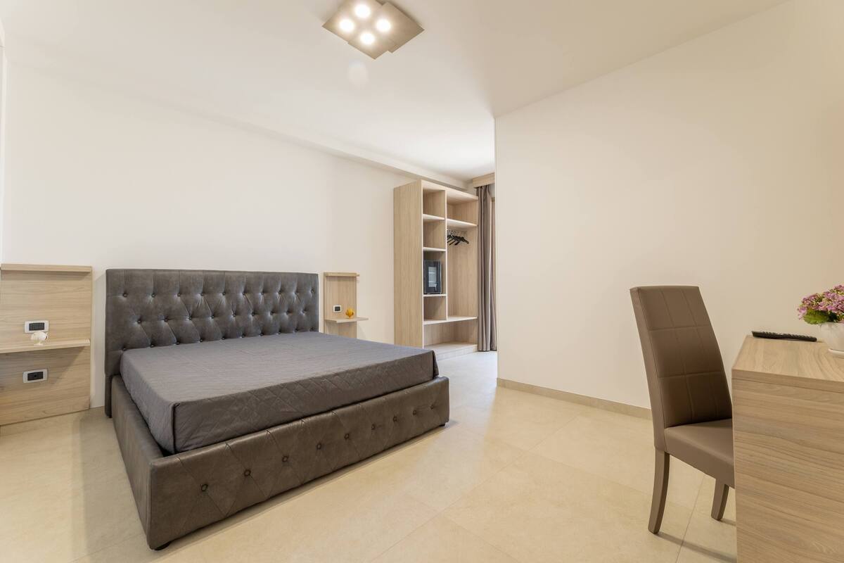 A modern bedroom with a large bed, a desk, and built-in shelving.