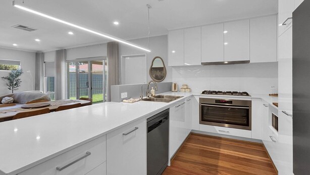 Una cocina moderna con armarios blancos, horno integrado y una isla grande con pileta.