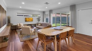 Una sala de estar moderna con una mesa de comedor de madera, sofás y un ventanal con vistas a un jardín.