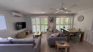 Una sala de estar moderna con sofá, mesa de centro, televisor y zona de comedor con sillas y una mesa.