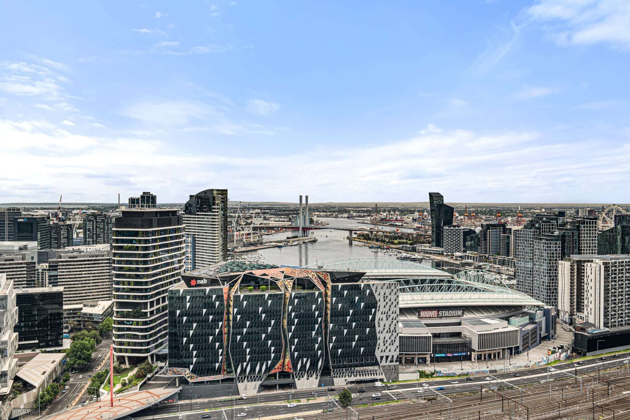 Un paisaje urbano moderno con un edificio destacado que presenta una fachada geométrica original y un estadio grande.