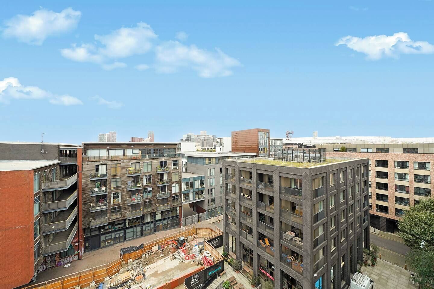 Ein mehrgeschossiges Gebäude mit Balkonen, einem Dachgarten und einer Baustelle im Vordergrund.