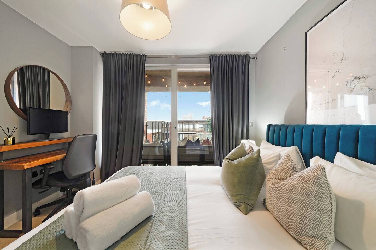 A hotel room with a bed, a desk with a computer, a chair, a window with curtains, and a view of the city.