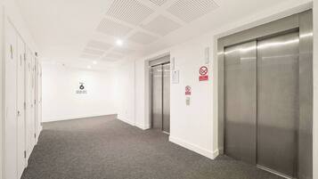 A hallway with a carpeted floor, white walls, and two elevators.