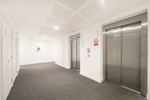 A hallway with a carpeted floor, white walls, and two elevators. - Stylish 1-Bed Apt with Balcony & Canal Views (Feltham)