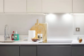 A modern kitchen with a stainless steel sink, a wooden pizza peel, and various kitchen items on the counter. - Stylish 1-Bed Apt with Balcony & Canal Views (Feltham)