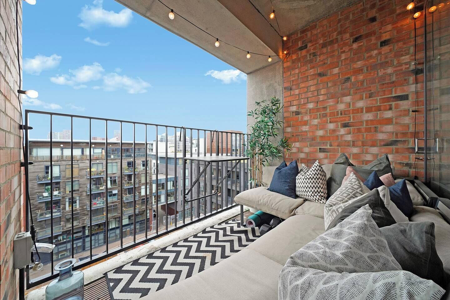 Un balcon avec un canapé, un tapis à motifs et un mur en briques.