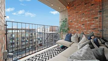 A balcony with a sofa, patterned rug, and a brick wall.
