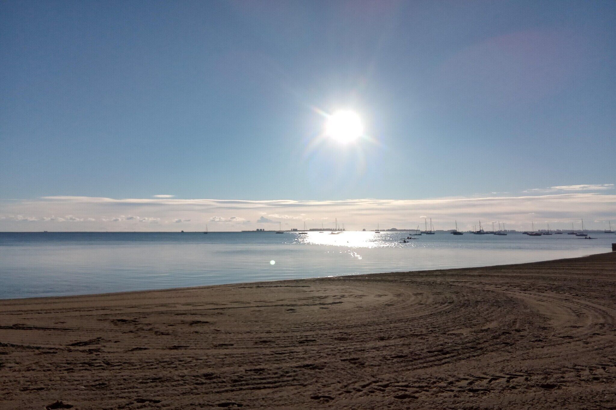 Una platja amb vaixells, cel blau i sol radiant.