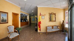 A lobby with a reception desk, a flag, a bench, a chair, and a large mirror.