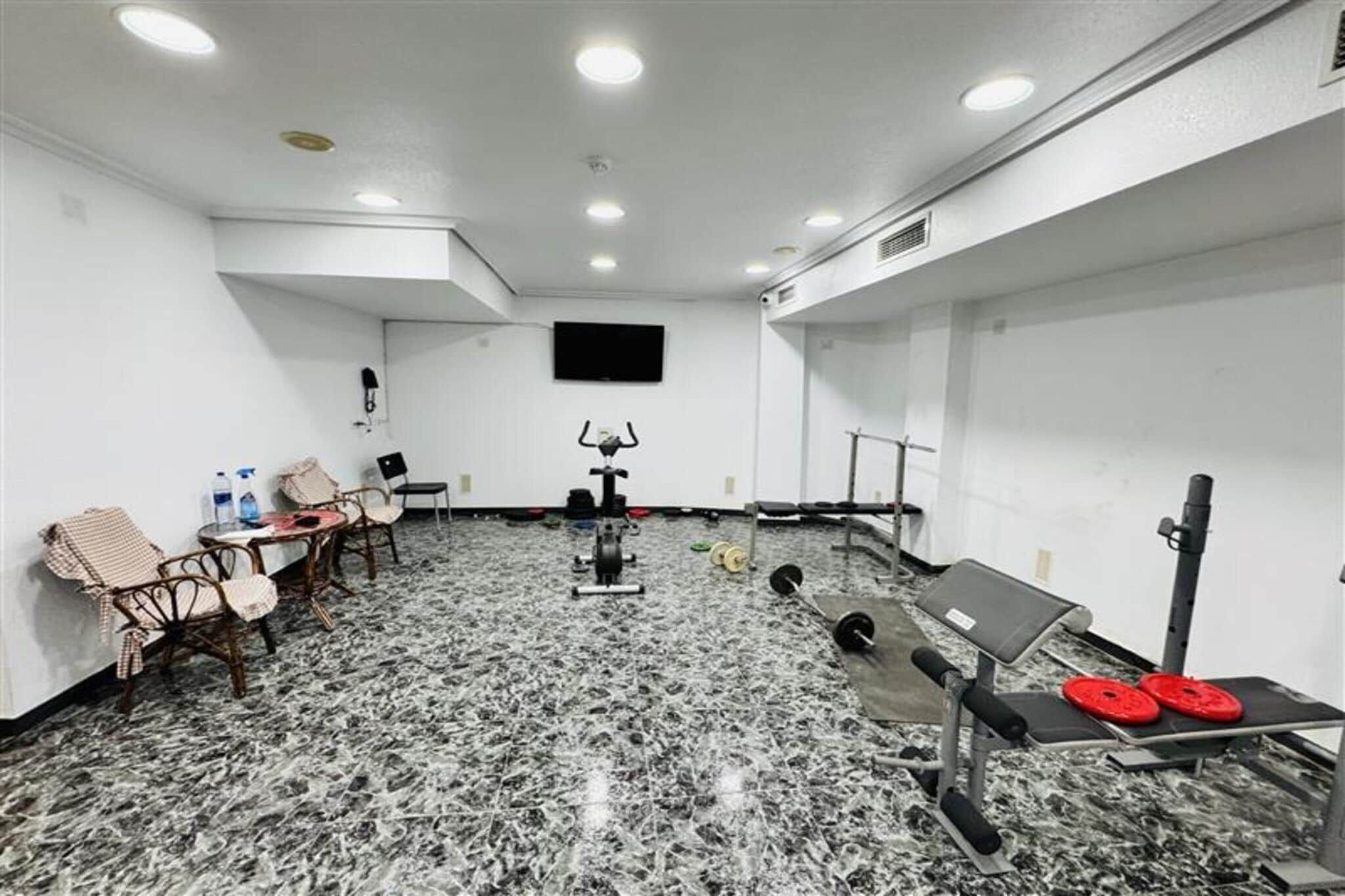 Un gimnasio con equipamiento de ejercicio, televisión y asientos.