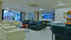 Eine moderne Hotelhalle mit Sitzbereichen, einem Empfangstresen und einem großen Fenster mit Blick ins Freie.