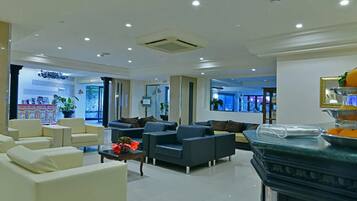 A modern hotel lobby with seating areas, a reception desk, and a large window offering a view of the outdoors.