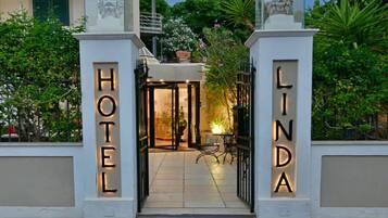 The entrance to a hotel with a well-lit sign and a small table with chairs outside.