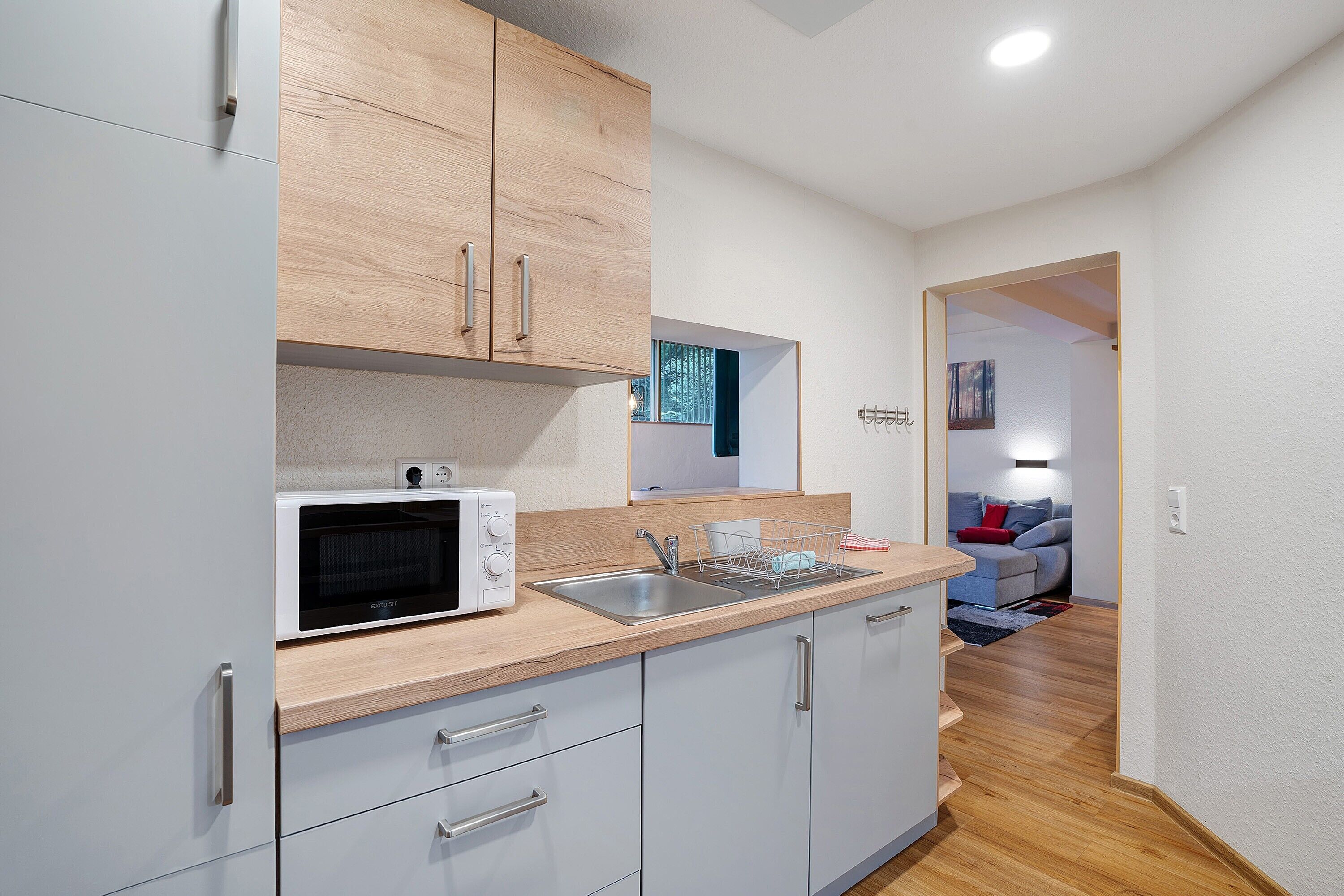 A compact kitchen with a microwave, sink, and wooden cabinets.