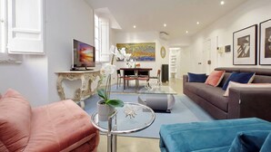 A modern living room with a sofa, a coffee table, and a TV. There is a dining area in the background with a table and chairs. - Amazing Apartment by the Pantheon (Rome)