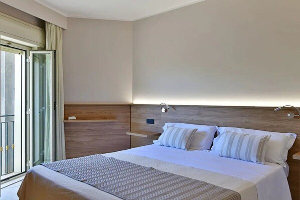 Habitació d'hotel amb un llit gran, un panell de fusta al capçal, una taula de nit i una finestra amb cortines.