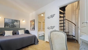 Ein Schlafzimmer mit Bett, Stuhl, Treppe und einem durchgegangenen Türrahmen sichtbarem Badezimmer.