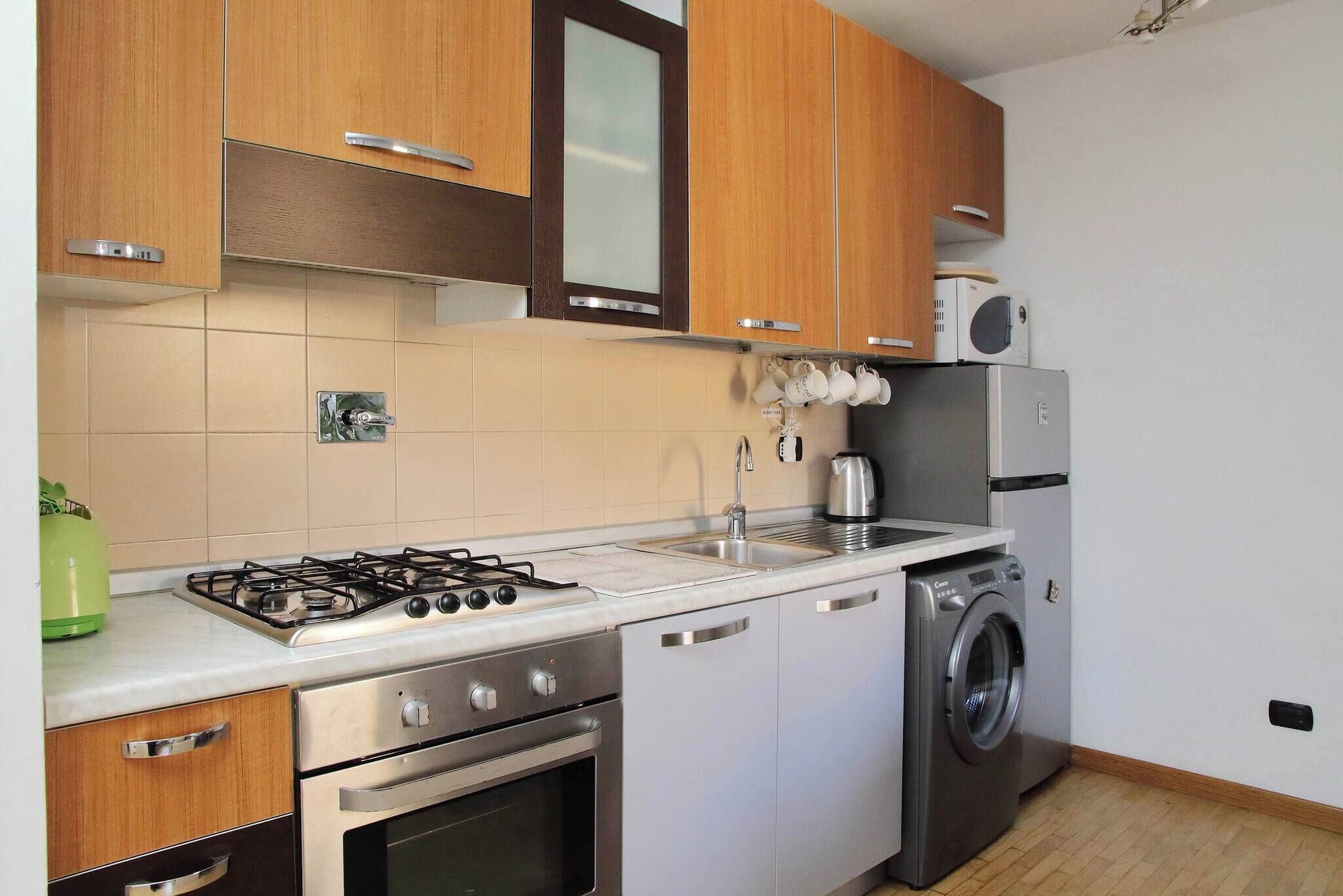 A compact kitchen with wooden cabinets, a gas stove, a built-in oven, a washing machine, and a microwave.