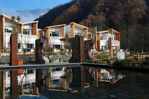 Un hotel moderno con varias construcciones, una piscina reflectante y un telón de fondo montañoso.