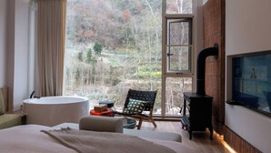 A modern bedroom with a large window, a bathtub, a chair, and a TV. - Old River Story Art Mountain Retreat (Mianyang)