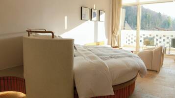A bedroom with a bed, a chair, a large window, and a view of the outdoors.
