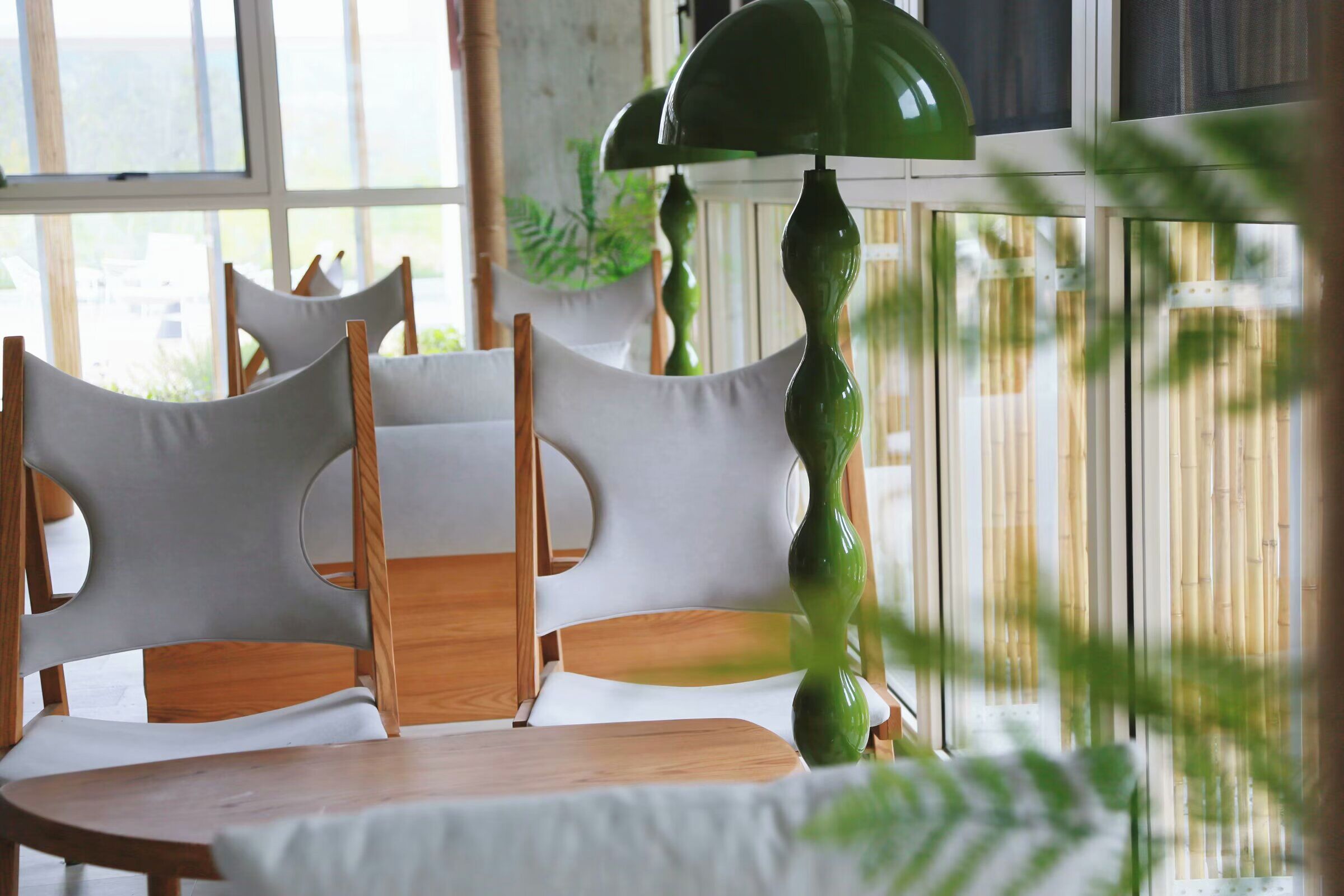 A dining area with a table and chairs, a hanging green lamp, and a bamboo fence in the background.