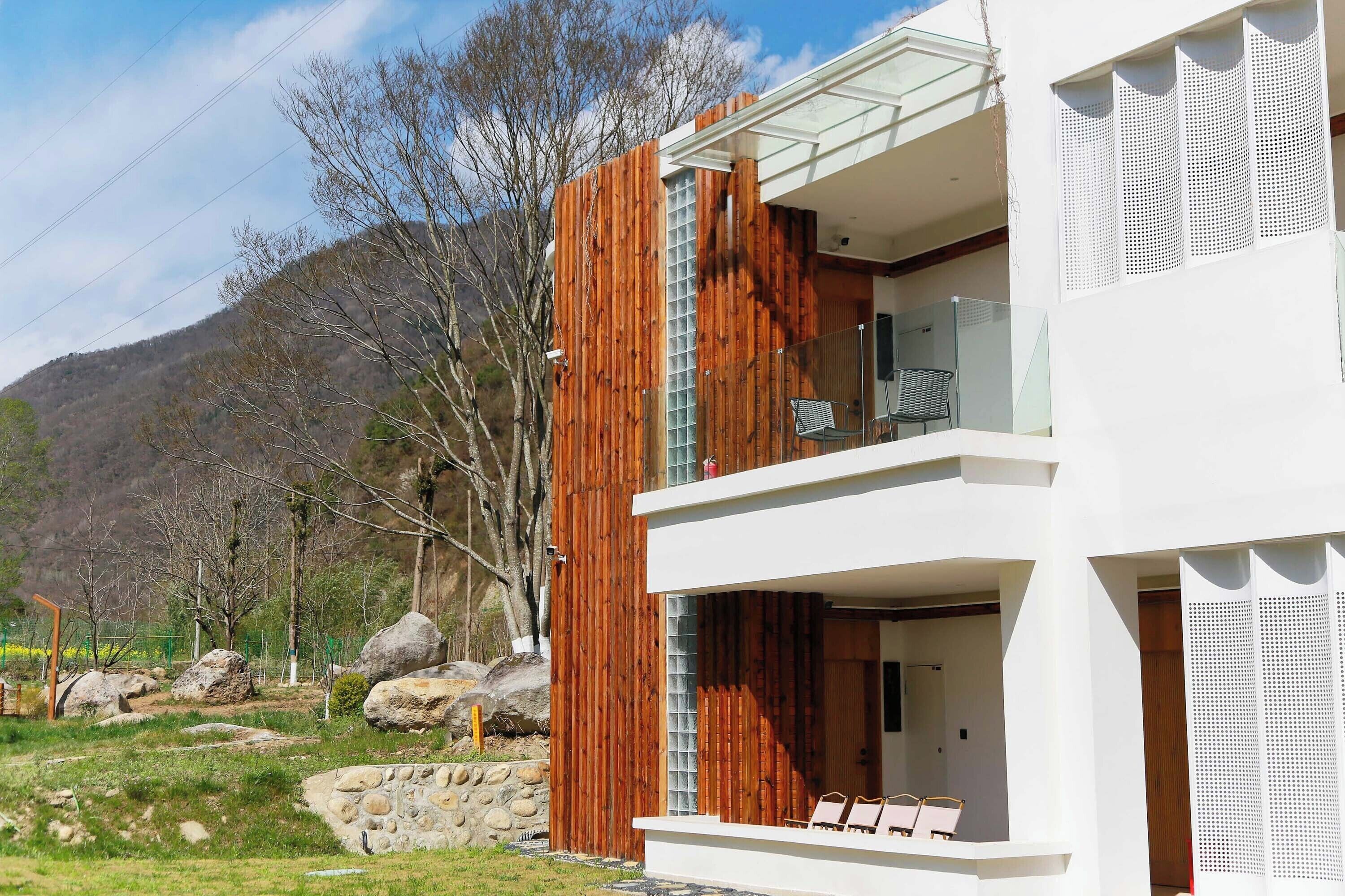 A modern building with a wooden facade, a balcony with chairs, and a view of a mountainous landscape.