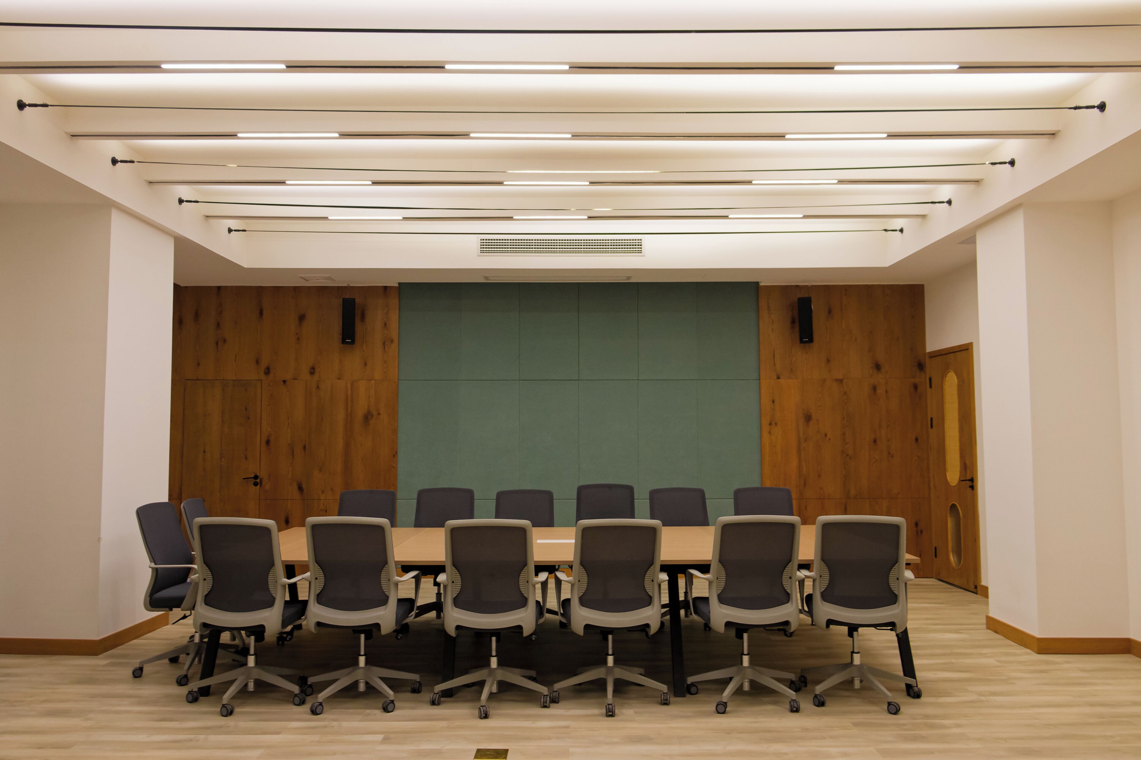 Une salle de conférence dotée d’une longue table et de chaises, de murs recouverts de panneaux en bois et d’un éclairage moderne.