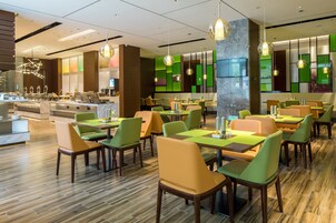 A modern restaurant with green and yellow chairs, wooden tables, and pendant lighting.
