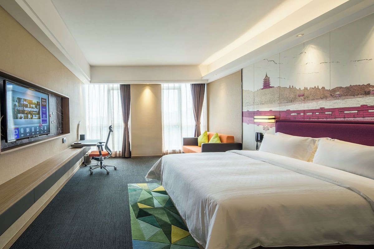 Une chambre d’hôtel avec un grand lit, un bureau, une chaise, une télévision et une fresque murale représentant un paysage urbain.