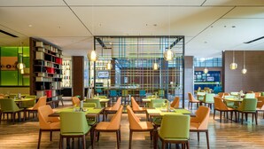 A spacious restaurant with multiple dining tables and chairs, a bar area, and a large bookshelf. - Hampton by Hilton Hangzhou Binjiang (Hangzhou)