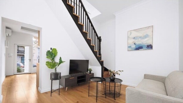 Un salon moderne avec un plancher en bois, un escalier, un téléviseur à écran plat, un canapé et un tableau accroché au mur.