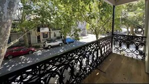 Un balcon doté d’une rambarde en métal, donnant sur une rue bordée de voitures garées et d’arbres.