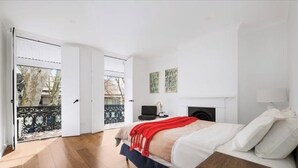Une chambre à coucher avec un lit, un bureau et une chaise. Il y a une fenêtre et une porte qui donne sur un balcon extérieur.