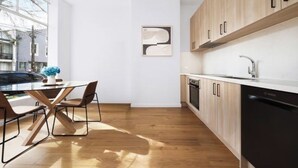 Une cuisine moderne avec des meubles en bois, un lave-vaisselle noir et un coin repas comprenant une table et des chaises en verre.