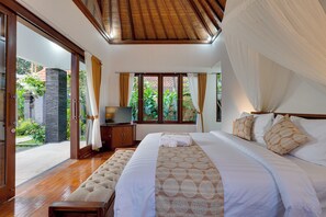 Ein Schlafzimmer mit einem großen Bett, einer Holzbank, einem Fernseher und Blick auf einen Garten durch Glastüren.