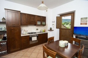 A kitchen with wooden cabinets, a stove, and a dining table with chairs. - APARTMENT OASIS THE PEARL - NATURE POOL AND GYM (Passignano sul Trasimeno)