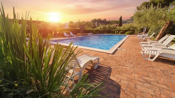 Piscina com espreguiçadeiras e vista para o pôr do sol.