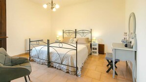 Quarto com uma cama de casal, mesas de cabeceira, uma cadeira, escrivaninha com espelho e um candelabro.
