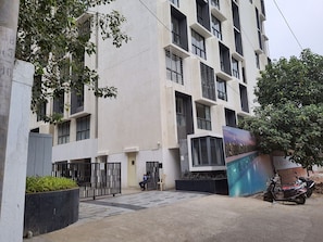A multi-story building with a modern architectural design, featuring a gated entrance and a parked scooter.