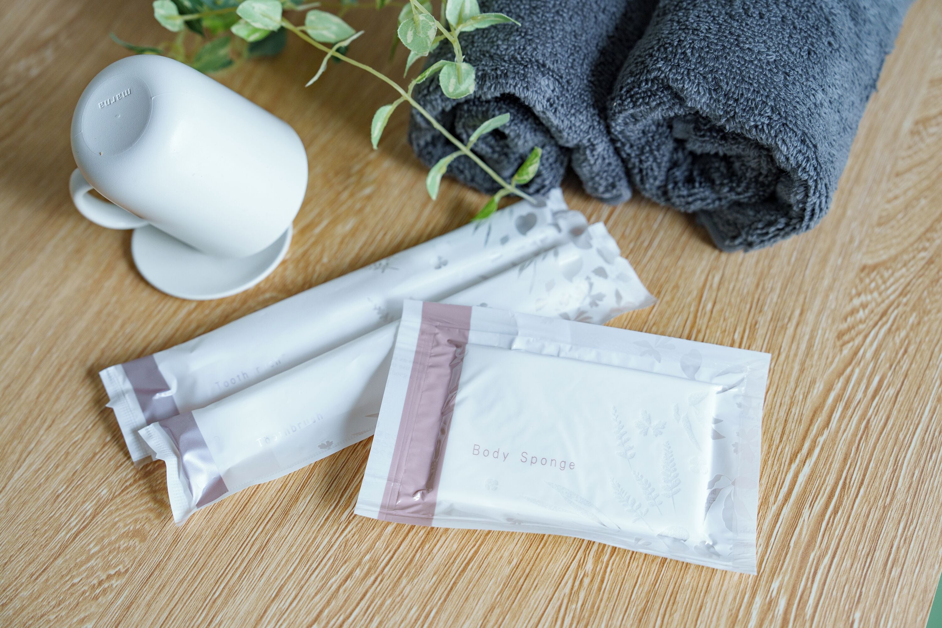 A wooden surface with a white mug, a rolled-up black towel, and two packages labeled "Body Sponge."