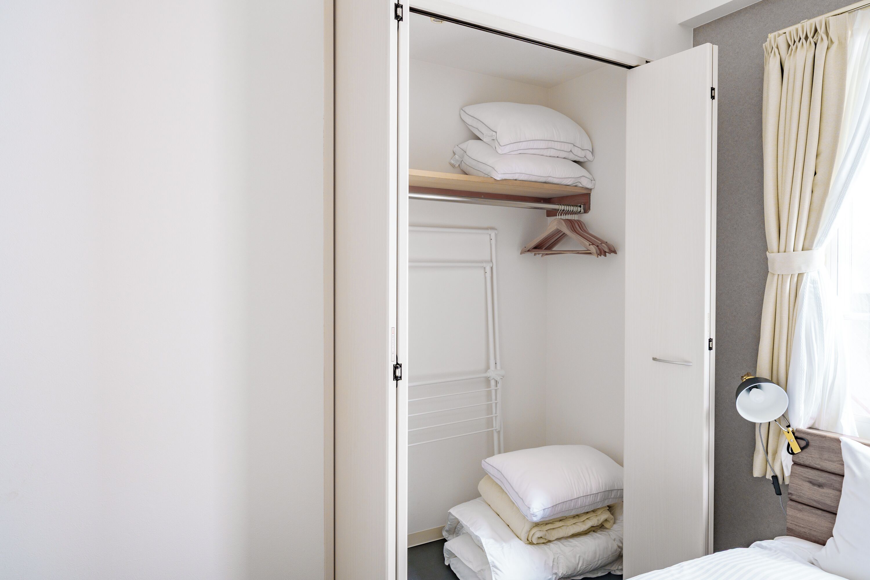 A neatly organized bedroom with a bed, a bedside table, a mirror, and a wardrobe.