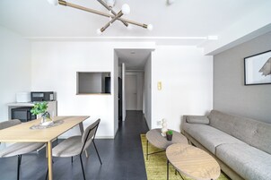 A modern living room with a sofa, a dining table with chairs, a coffee table, and a TV mounted on the wall.