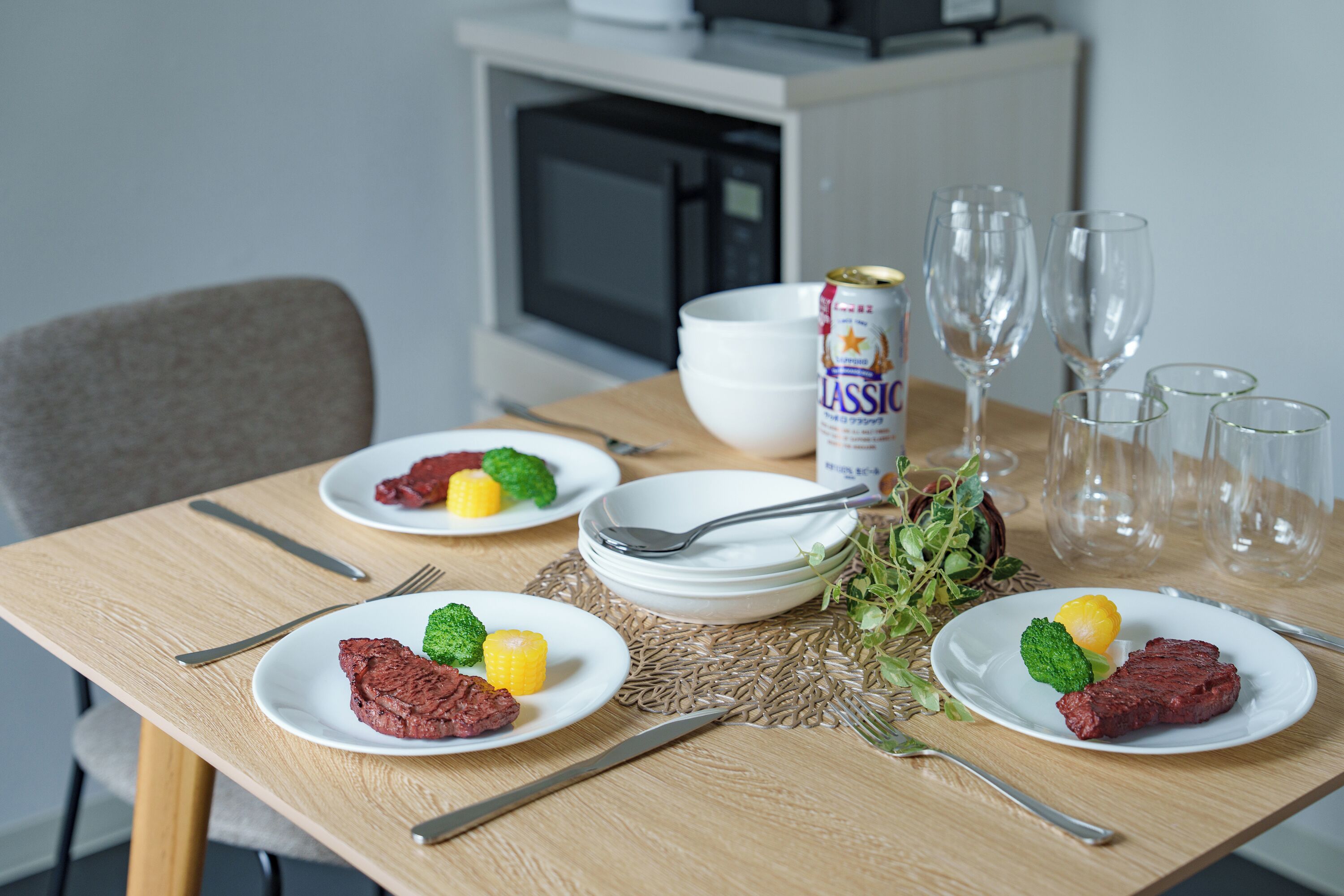 A dining table with plates of food, cutlery, and a can of beer.