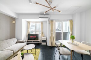 A modern living room with a sofa, a dining table with chairs, a TV, and an air conditioning unit.
