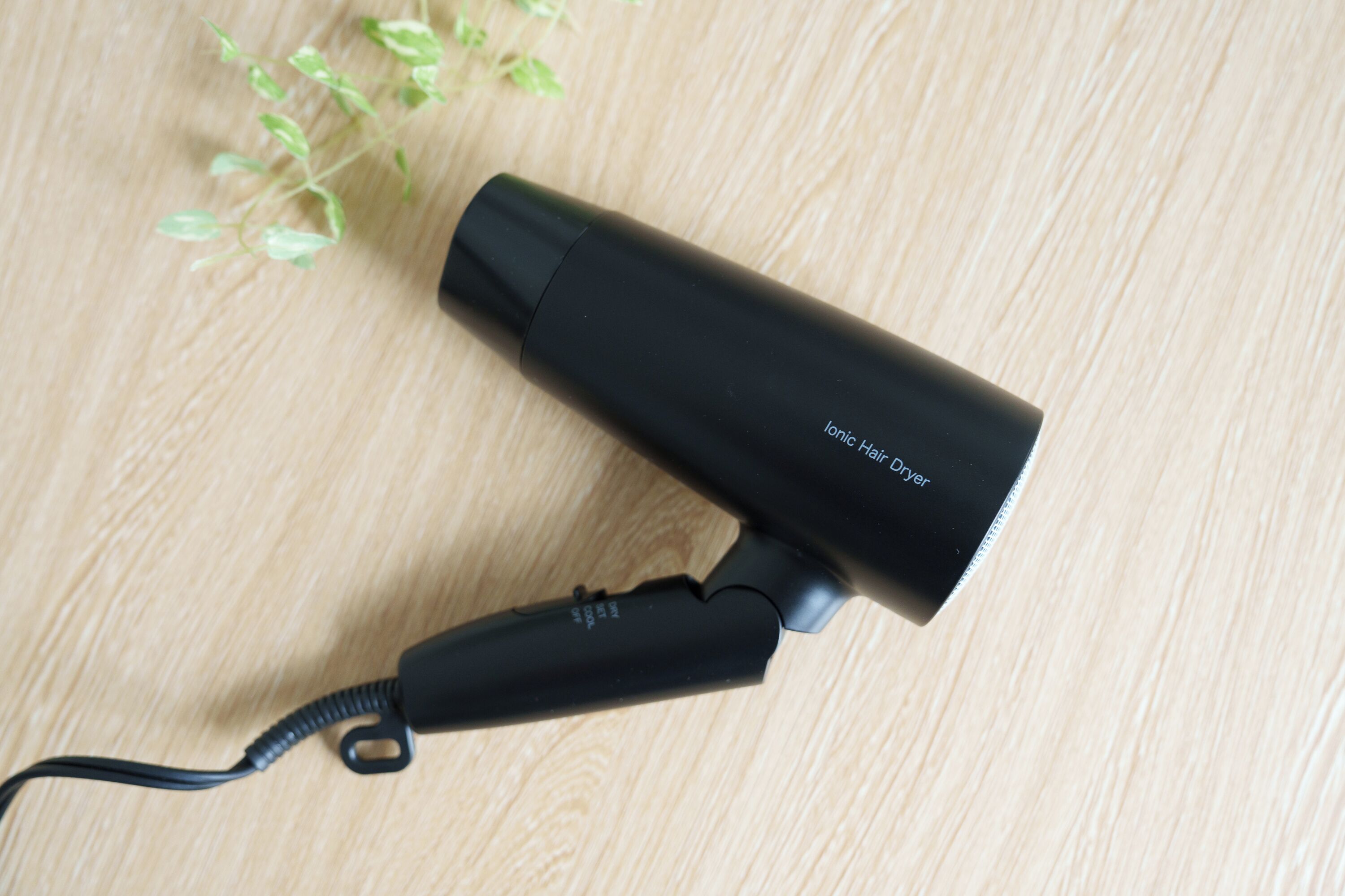 Un sèche-cheveux noir avec un cordon, posé sur une surface en bois.